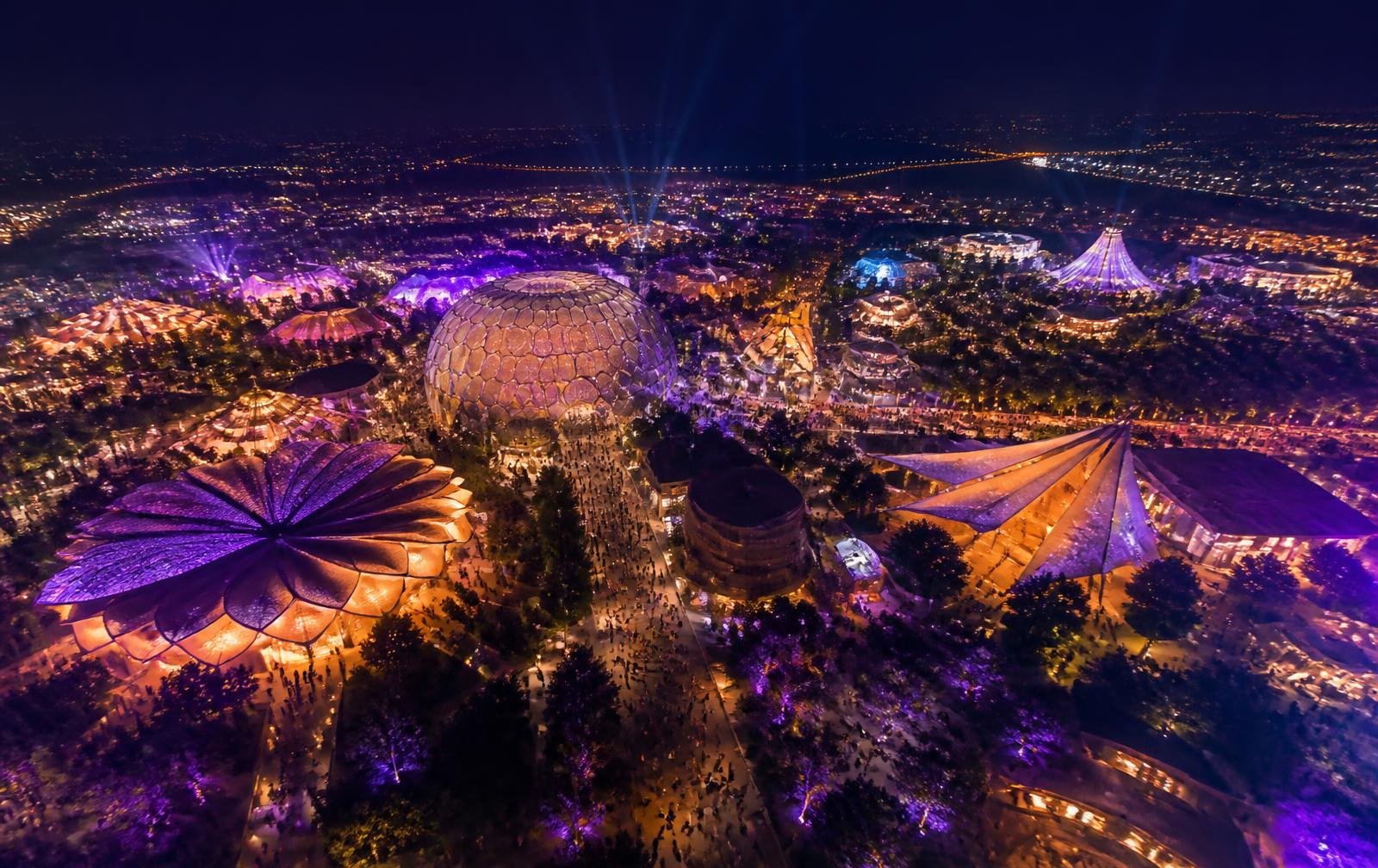 Aerial view of a global festival campus at night, lit in purple and amber